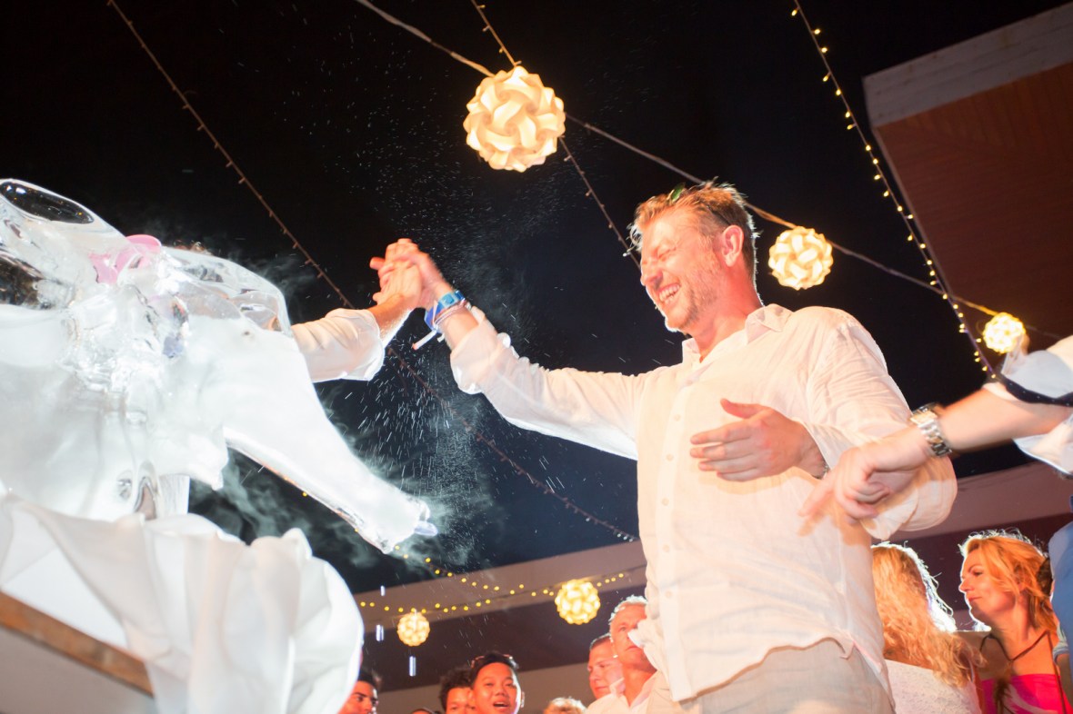 A joyful wedding celebration featuring a man in a light-colored shirt interacting with guests, with decorations and string lights in the background.