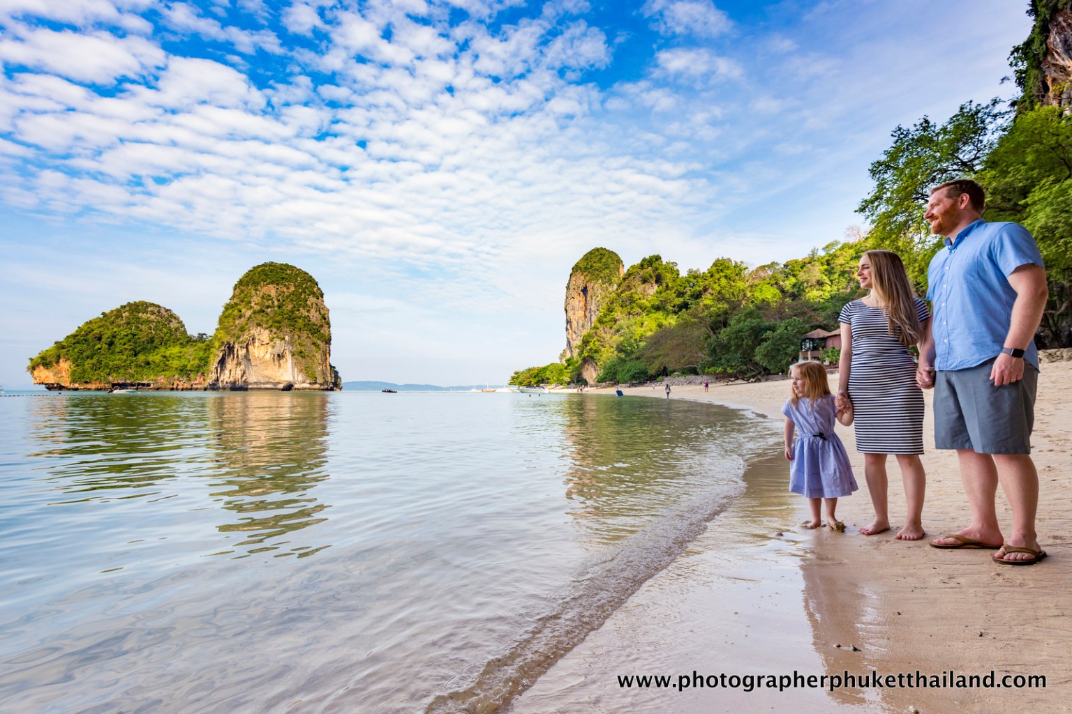 Family standing on the beach at Krabi, Thailand, with limestone cliffs in the background and calm waters.