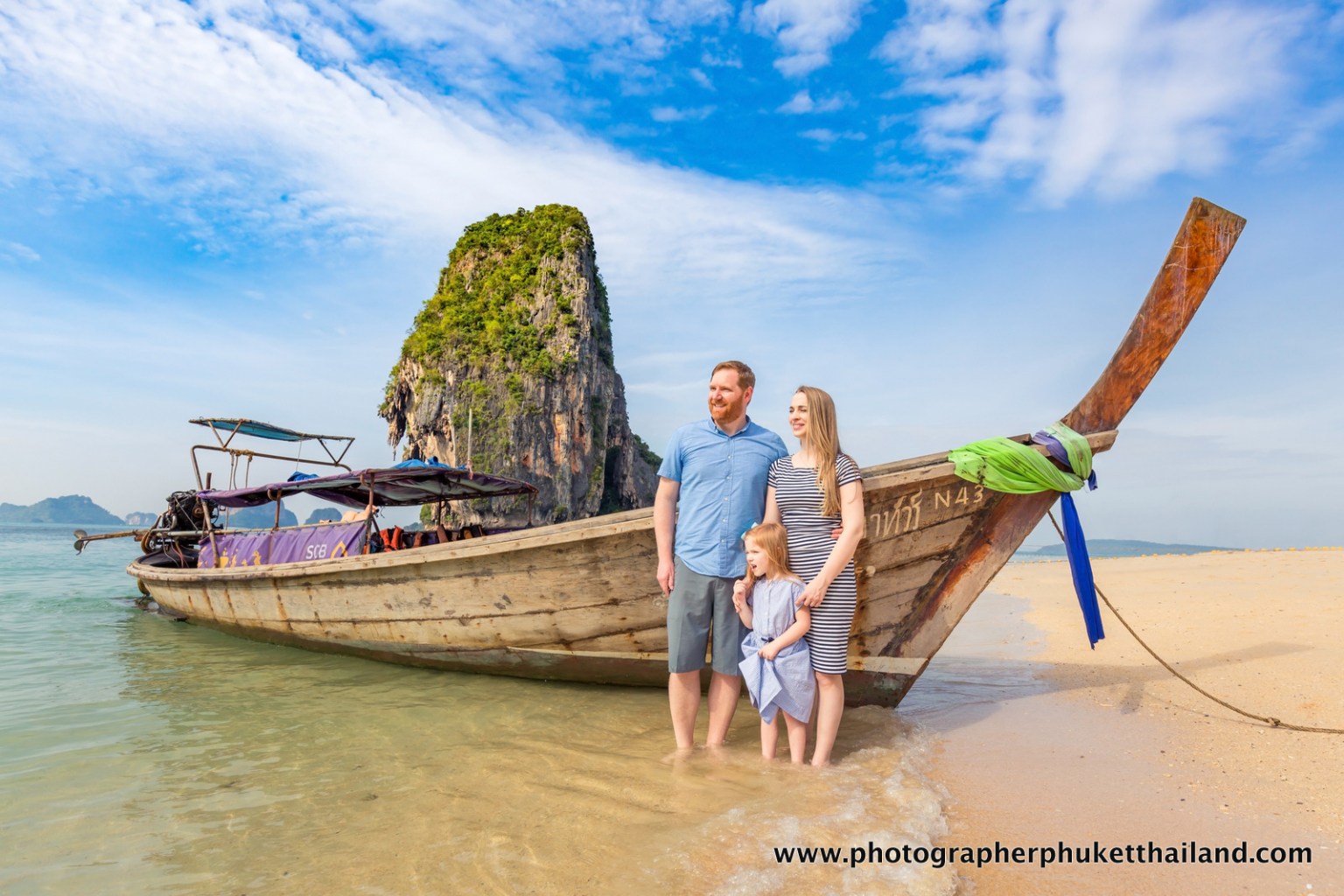 Family standing on the beach next to a traditional Thai long-tail boat, with a limestone cliff in the background.