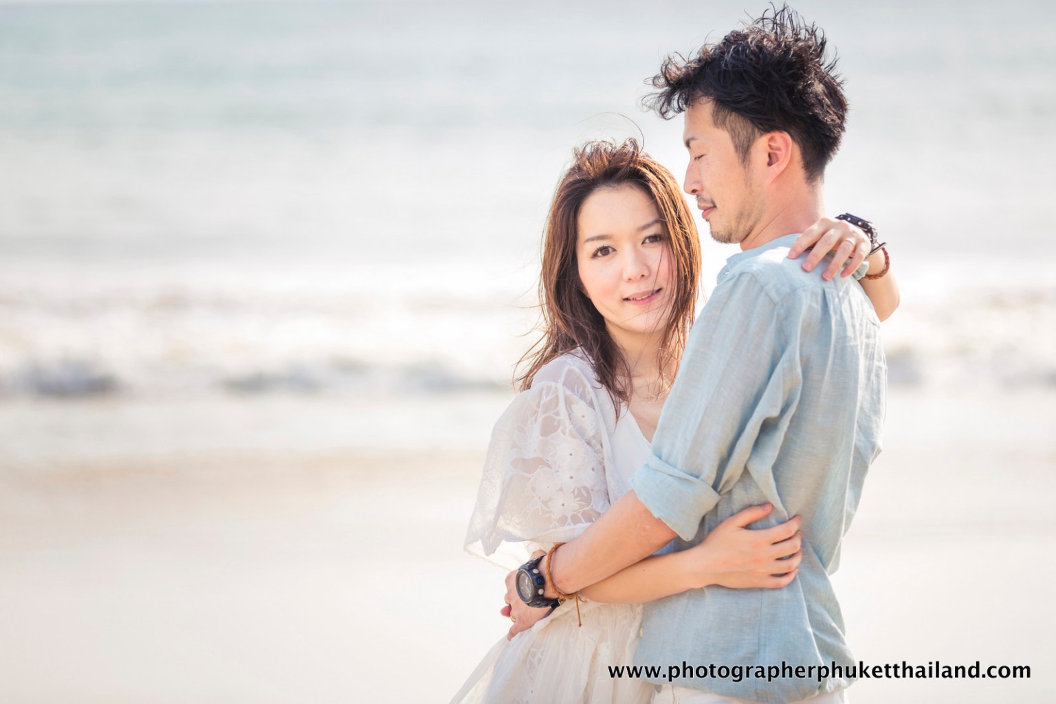 A couple embracing on the beach, with the ocean in the background and a soft, dreamy atmosphere.