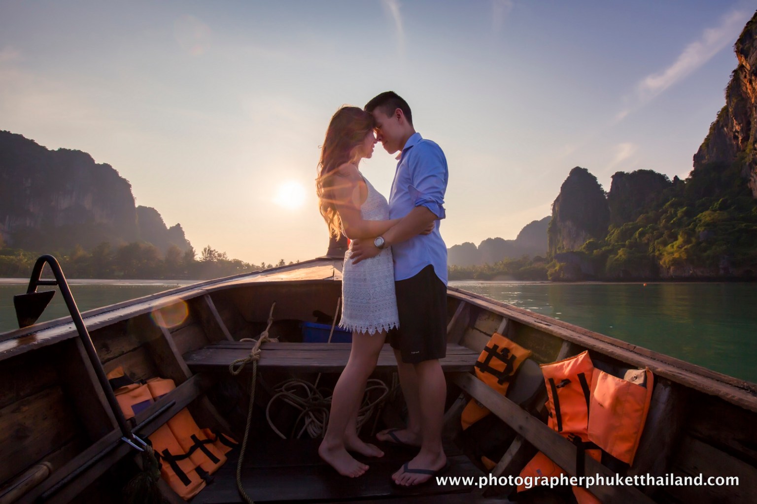 A couple embraces on a boat during sunset in Krabi, Thailand, with limestone cliffs in the background.
