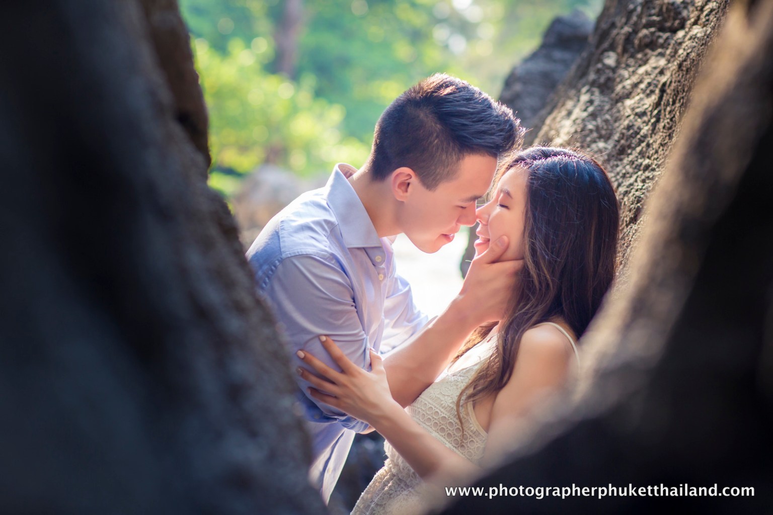 A couple sharing a romantic moment, close to each other, with sunlight filtering through trees in the background.