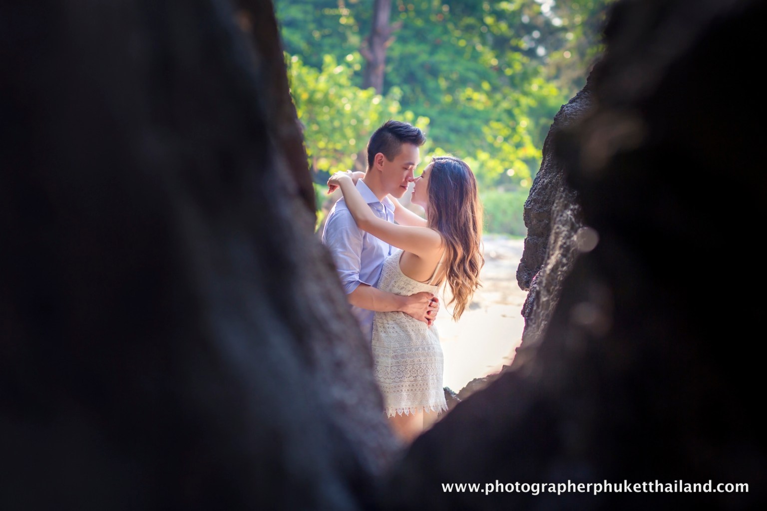 A couple embraces in a romantic pose, framed by rocky formations, with a backdrop of greenery in Krabi, Thailand.