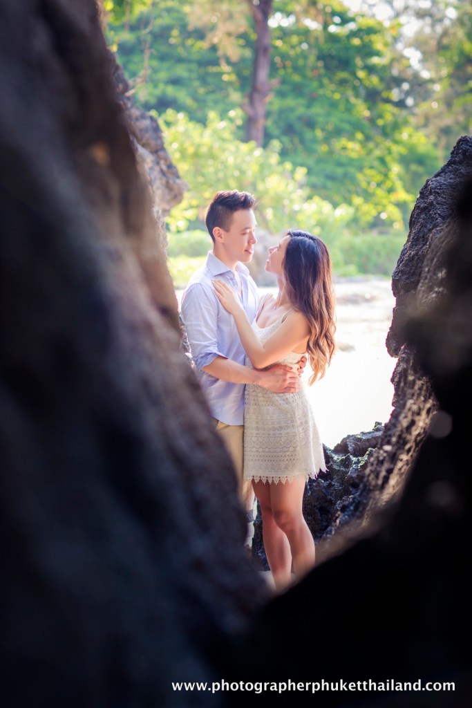 A couple embracing near the shoreline, framed by rocky formations in Krabi, Thailand.