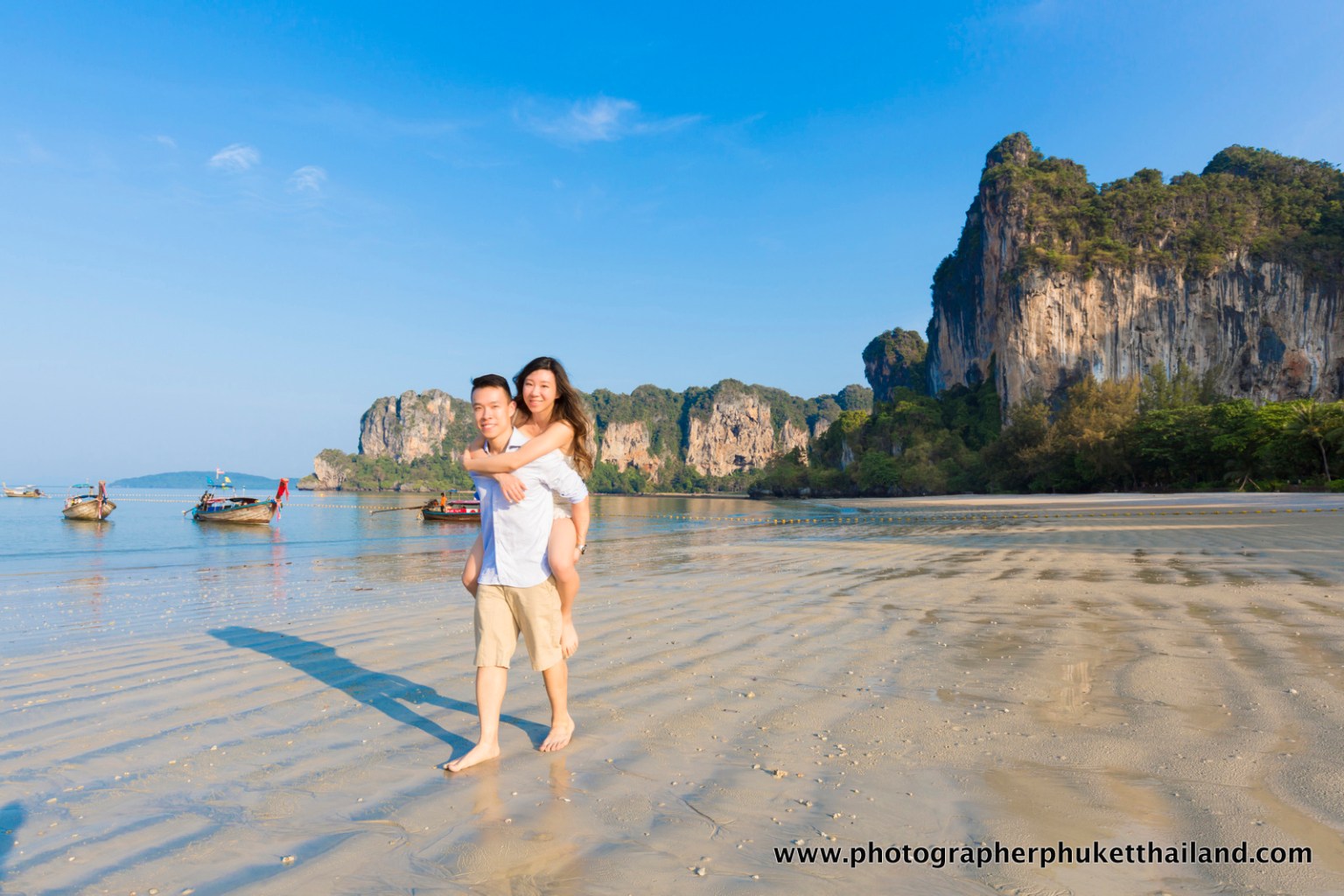 A couple enjoying a romantic moment on the beach in Krabi, Thailand, with limestone cliffs in the background.