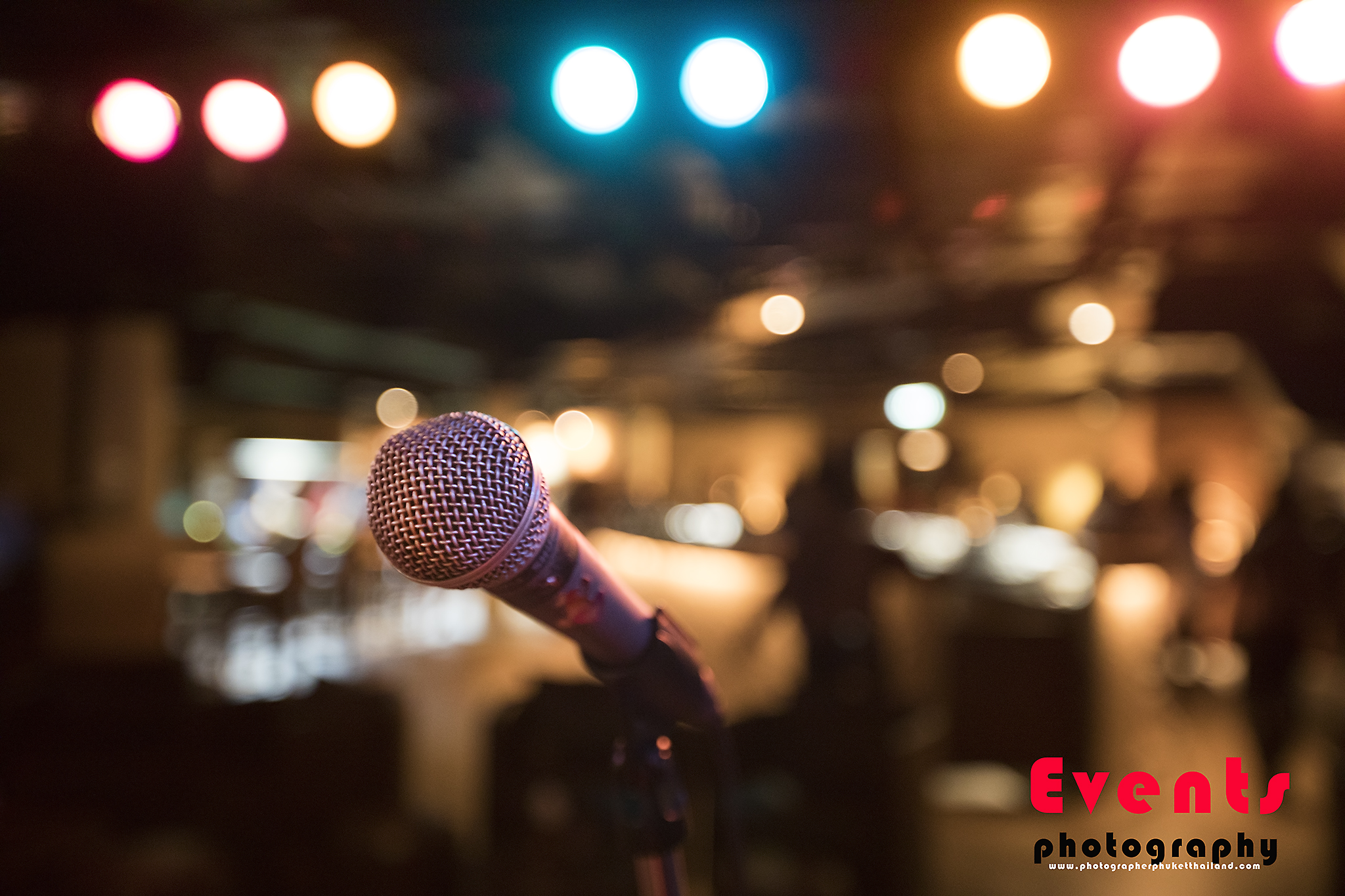 Close-up of a microphone with colorful stage lights in the background, indicating a live event or performance setting.