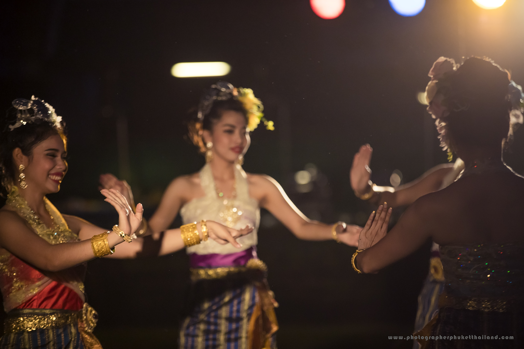 Three women in traditional Thai clothing perform a traditional dance at night in welcome corporate meeting party for , illuminated by soft stage lights.