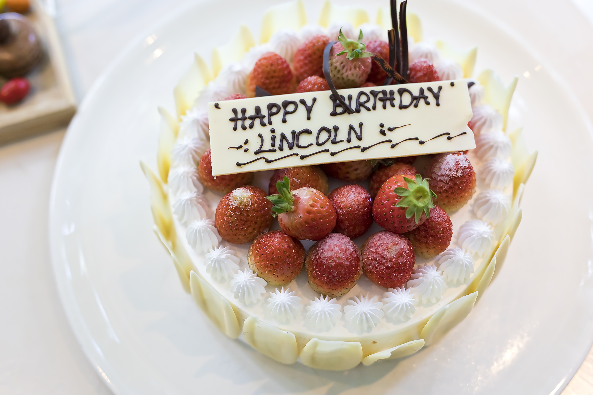 A decorated birthday cake with strawberries and a chocolate message that reads 'HAPPY BIRTHDAY LINCOLN'.