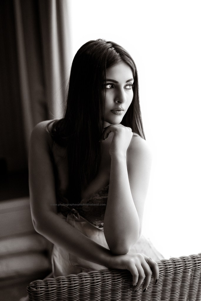 Black and white portrait of a woman sitting with her chin resting on her hand, gazing thoughtfully out of a window.