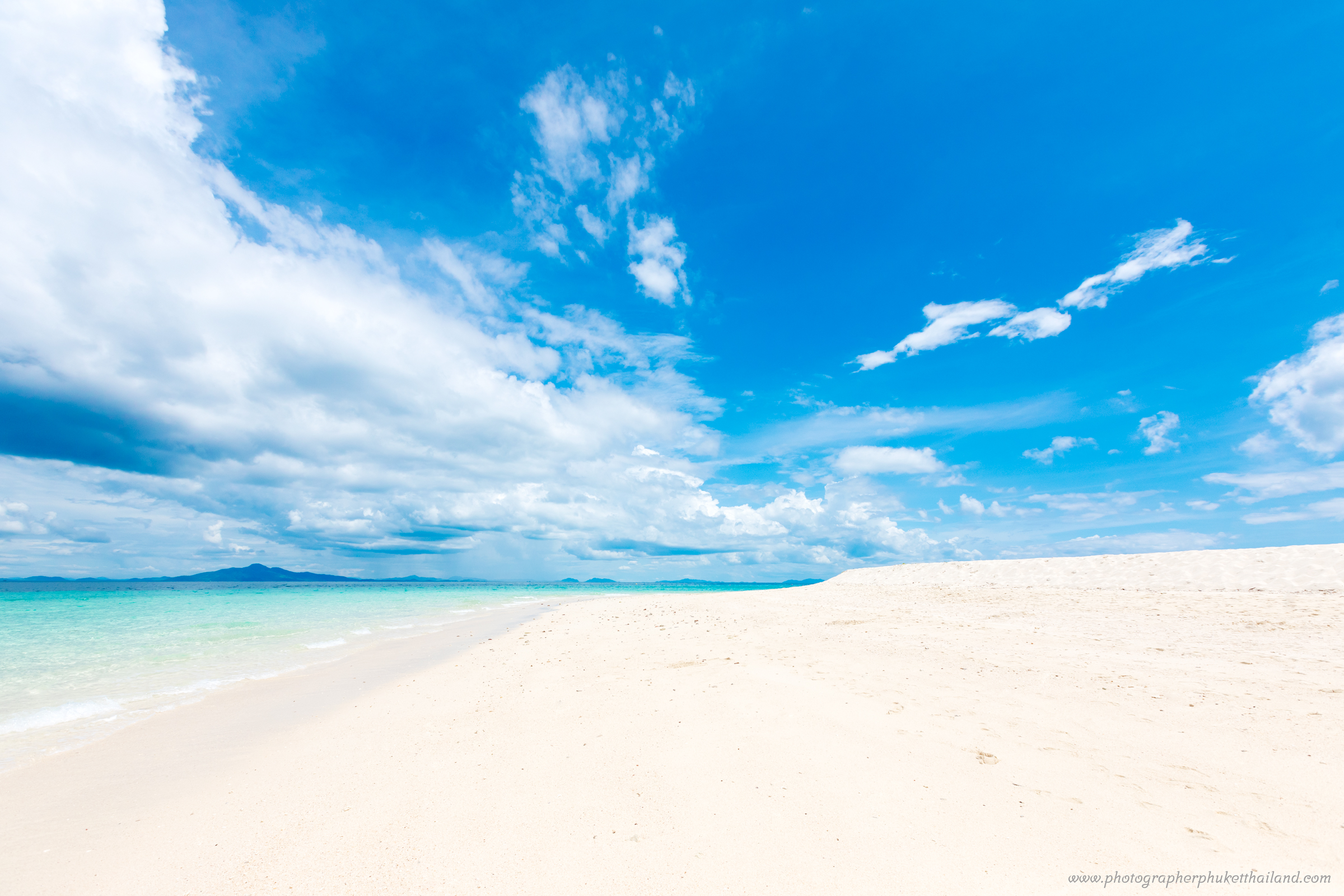 A beautiful beach scene with white sand and clear turquoise water under a bright blue sky with fluffy white clouds at bamboo island phi phi krabi..