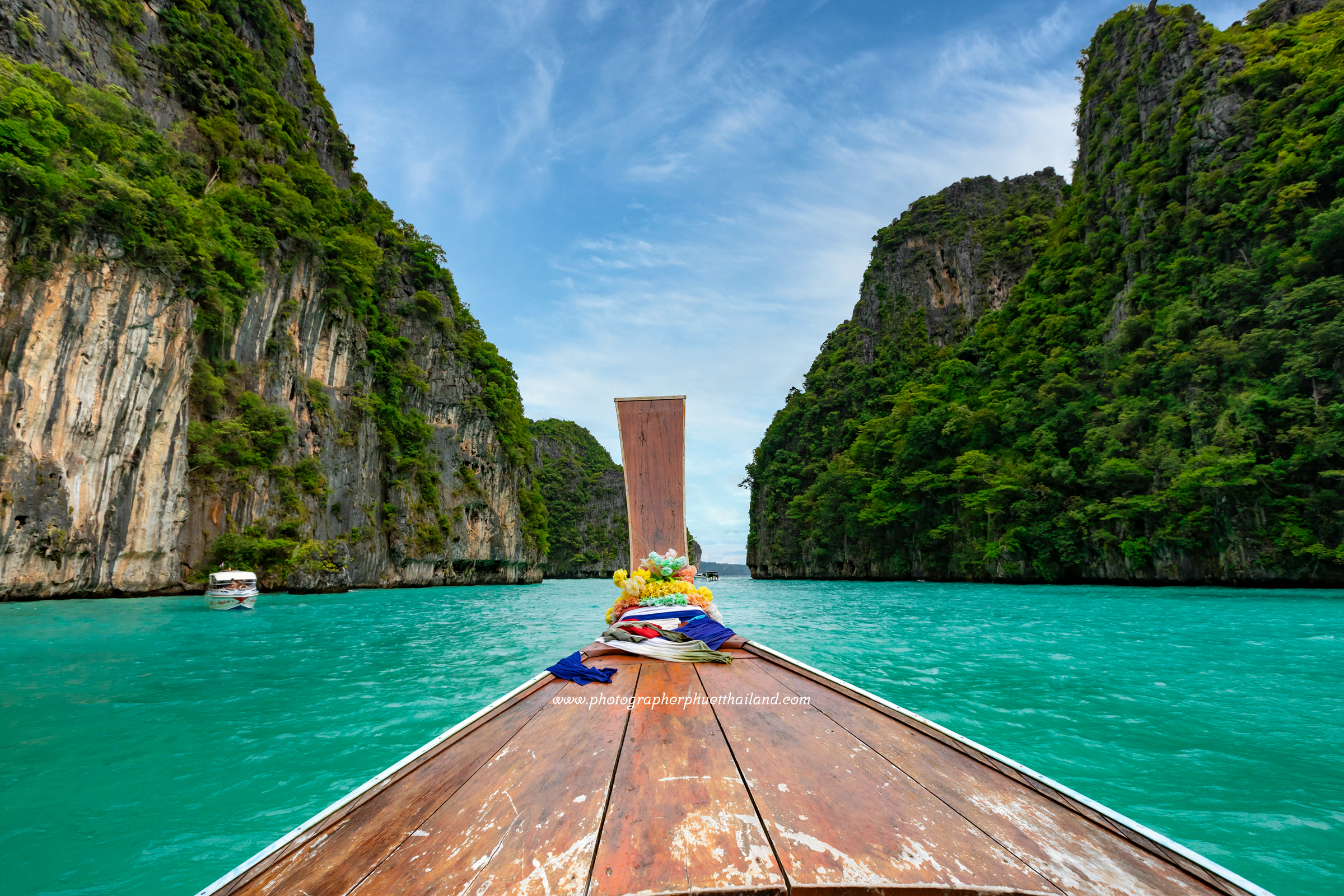 View from a long-tail boat navigating through the turquoise waters of Pileh Lagoon, surrounded by lush greenery and towering cliffs.