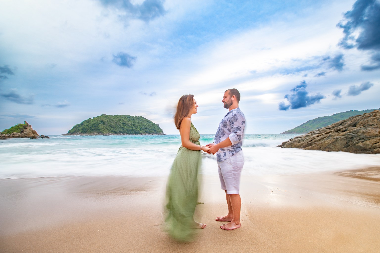 Couple holding hands on the beach at Ya Nui Beach, Phuket, with waves in the background.