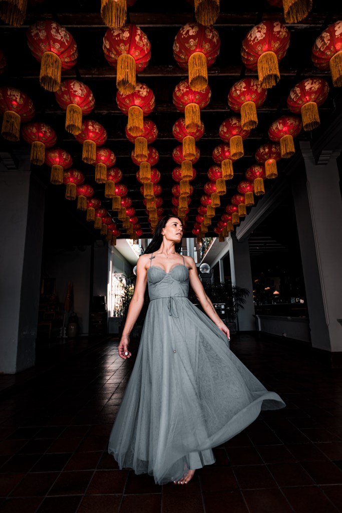 A model wearing a flowing gray dress poses under vibrant red lanterns, capturing a moment in a stylish setting.