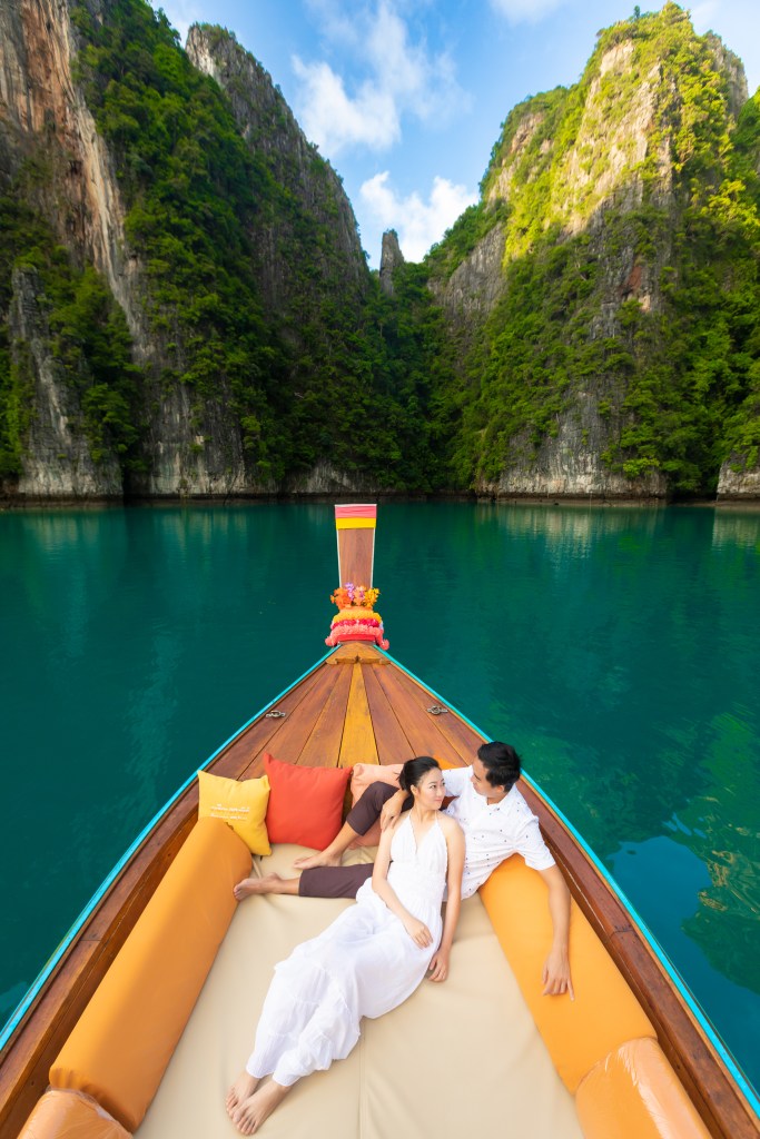 A couple relaxing on a boat surrounded by lush cliffs and turquoise waters.