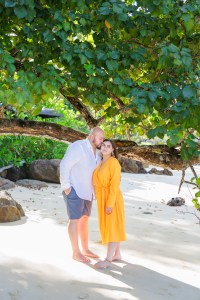 Honeymoon couple photo shoot at Banyan tree Krabi . A couple standing close together under a tree at the beach, with one person in a white shirt and the other in a bright orange dress, both smiling.