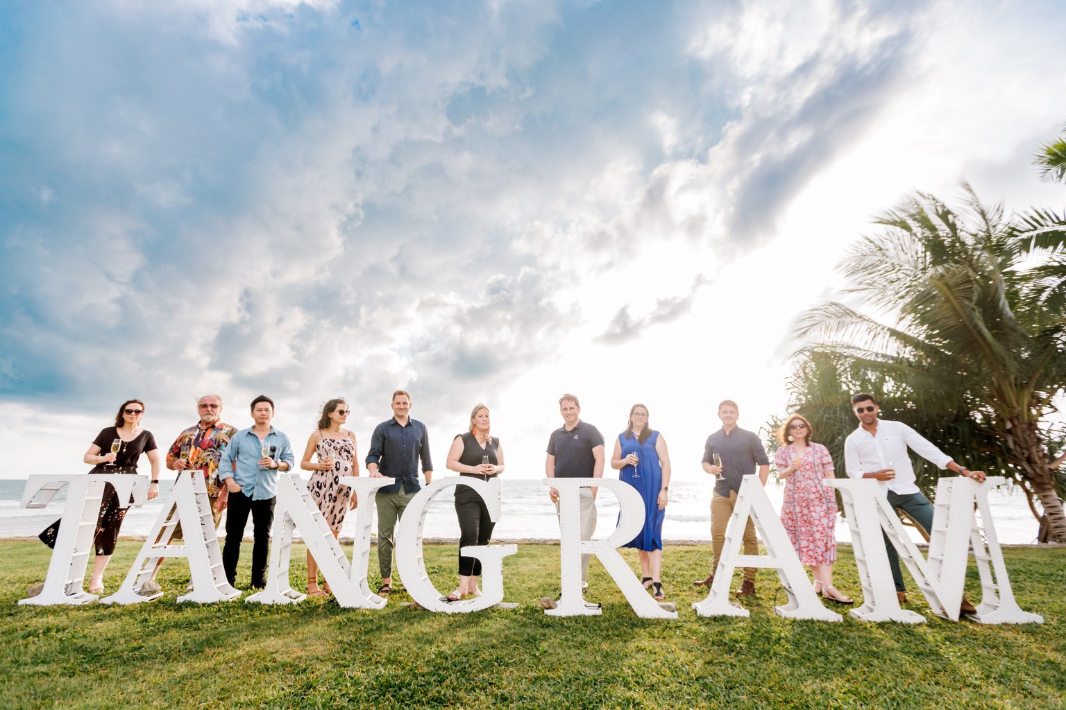 Group of people posing with large letters spelling 'TANGRAM' at a seaside event.