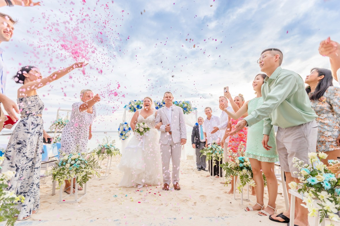 A joyful wedding moment with the bride and groom walking down the aisle, surrounded by guests throwing pink flower petals.