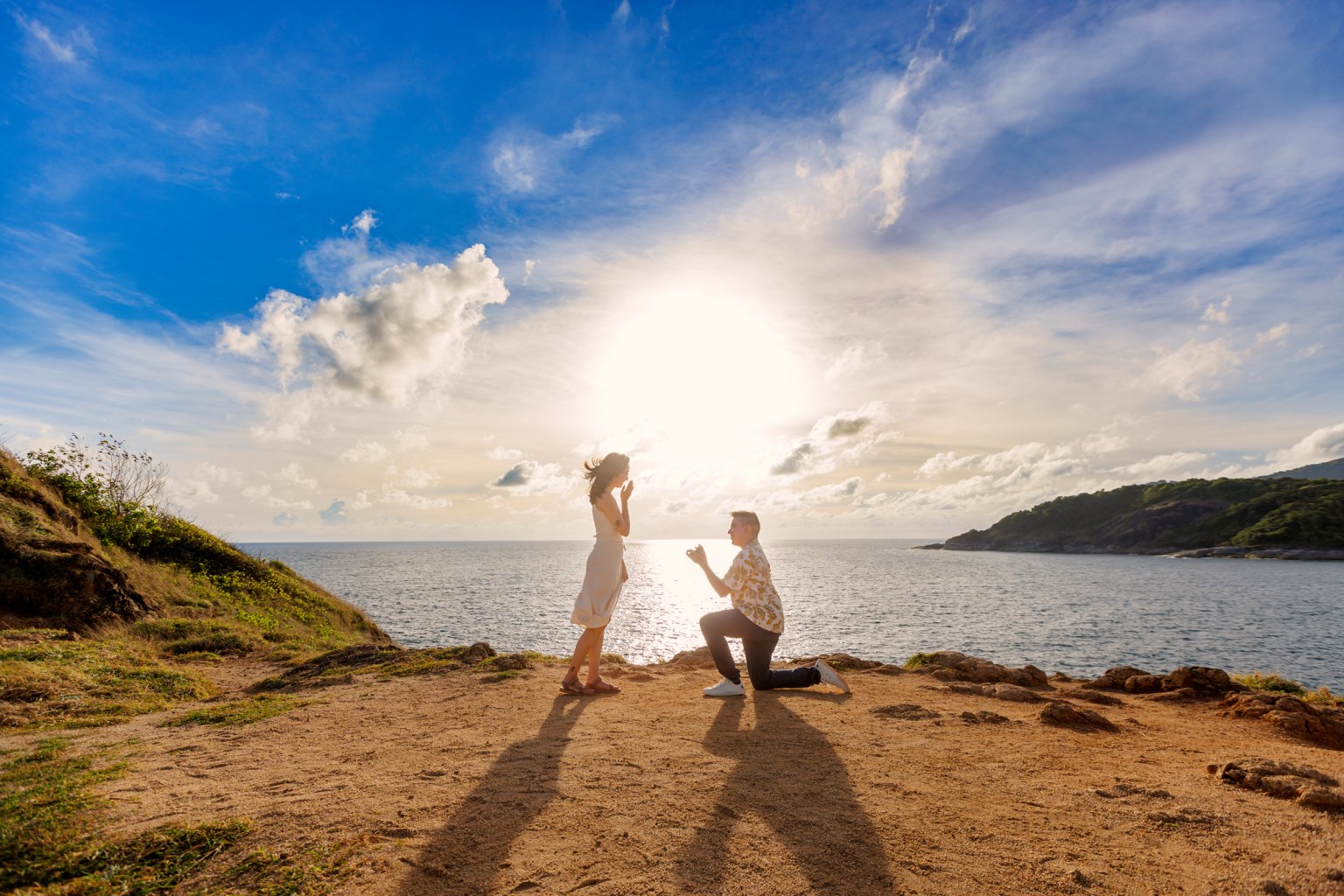 A couple at Promthep Cape, Phuket, captured during a romantic proposal at sunset, with the ocean and clouds in the background.