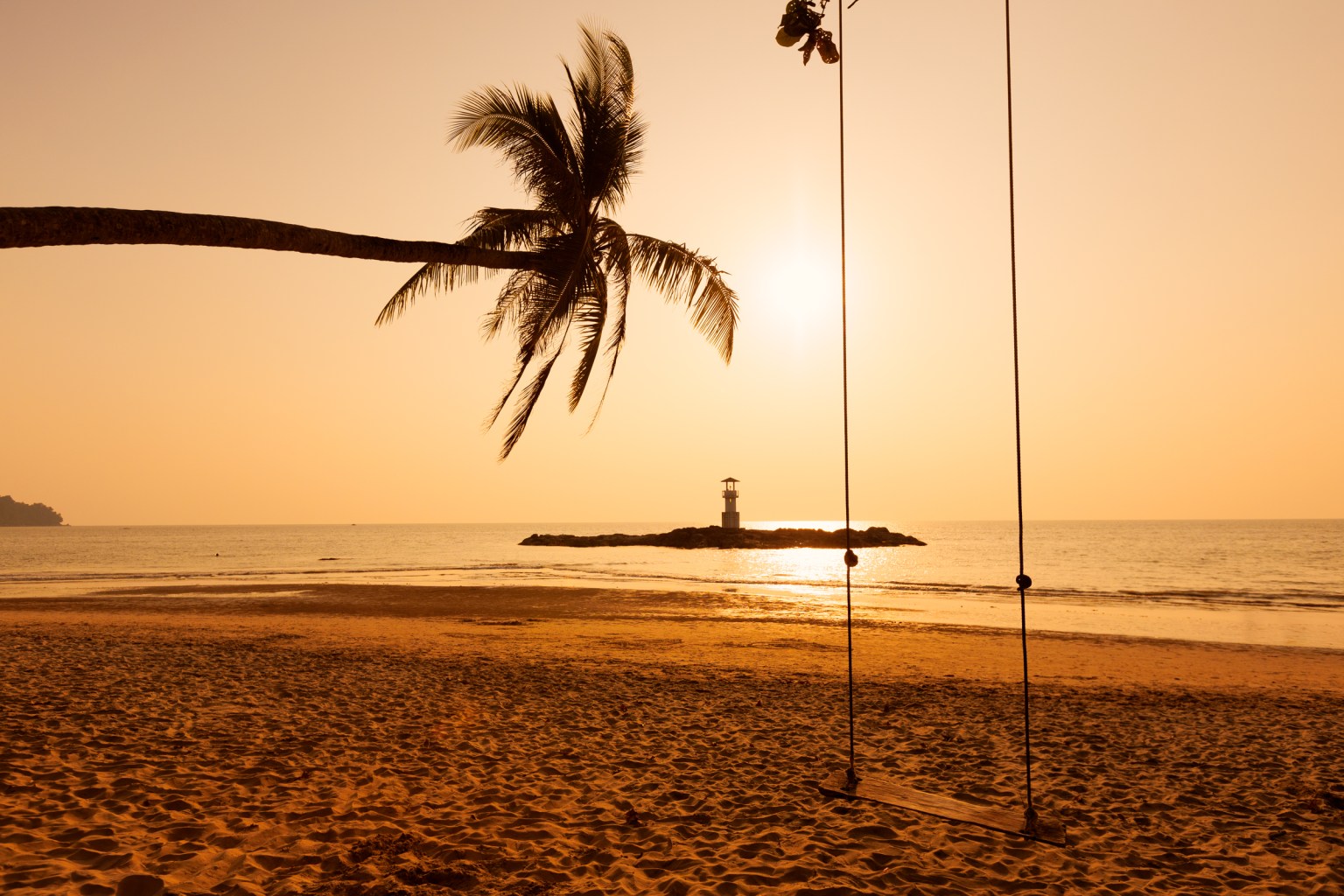 Sunset view over a Khao Lak beach with a swing and palm tree, highlighting a serene atmosphere.