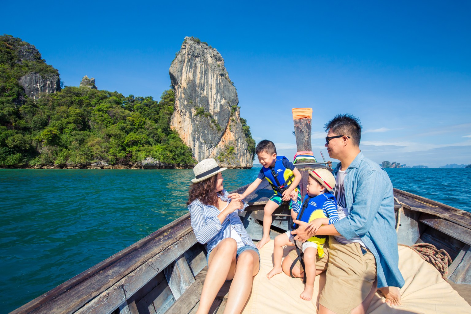 A family enjoying a day on a boat in Krabi, Thailand, with lush limestone cliffs in the background.