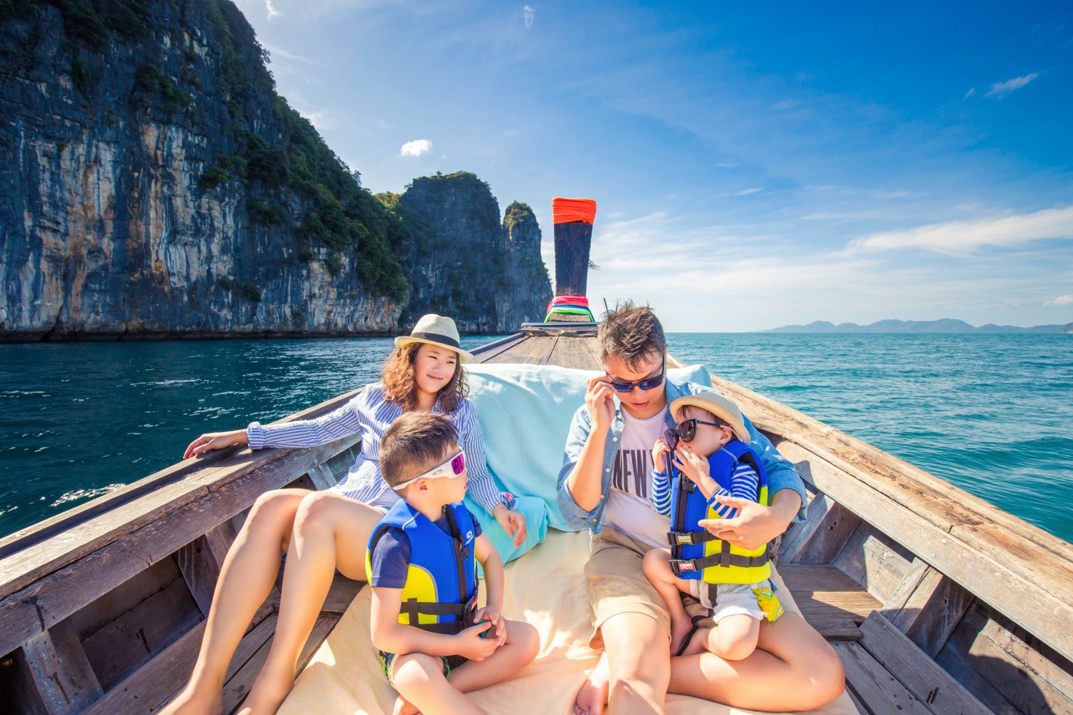A family enjoying a boat ride in Krabi, Thailand, surrounded by limestone cliffs and a clear blue sky.
