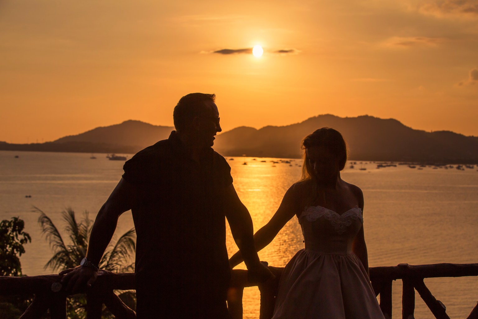 Silhouette of a couple holding hands at sunset over a serene beach, with mountains in the background.