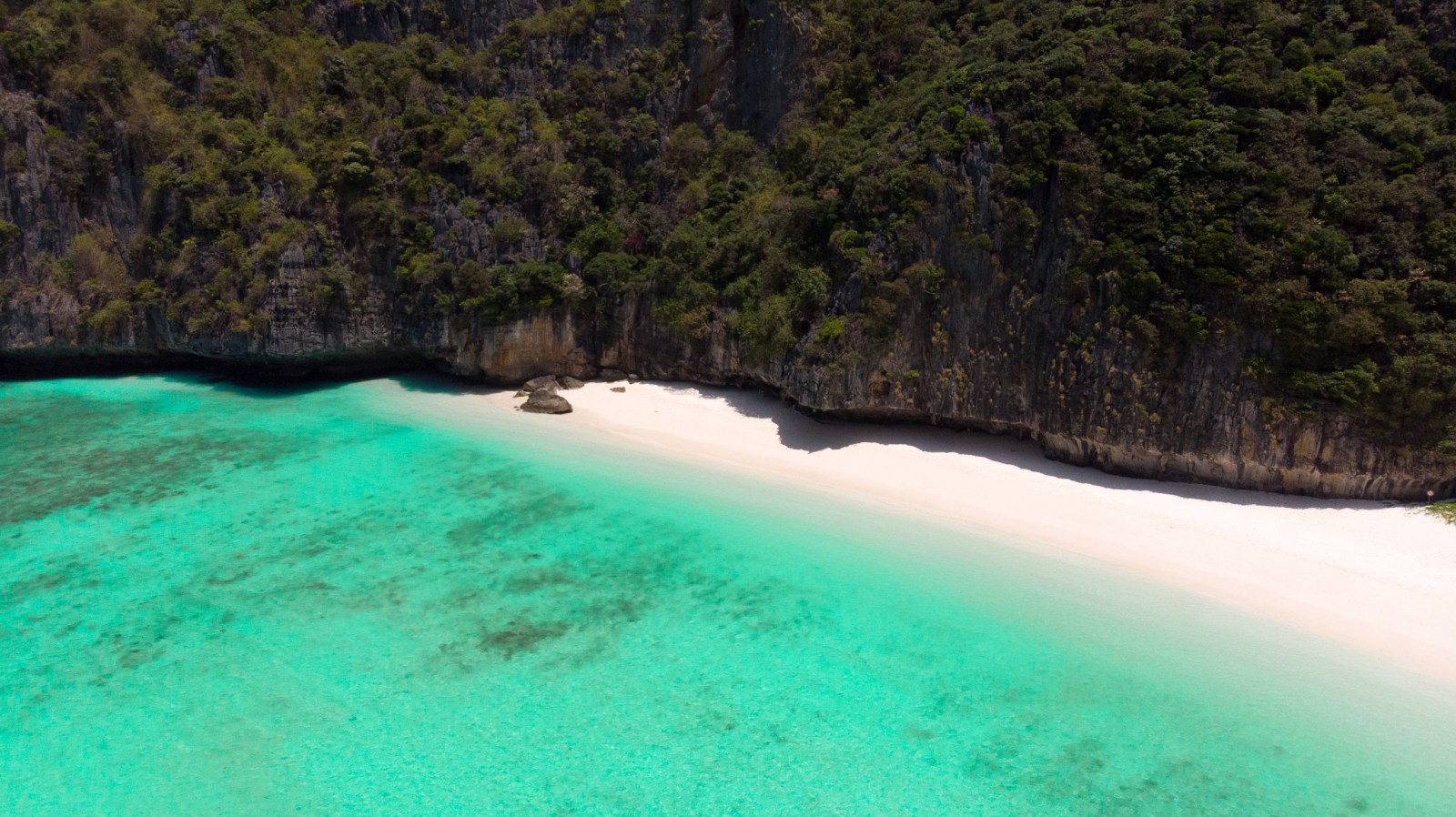 Aerial view of Maya Bay showcasing its turquoise waters, sandy beach, and lush limestone cliffs in Thailand.