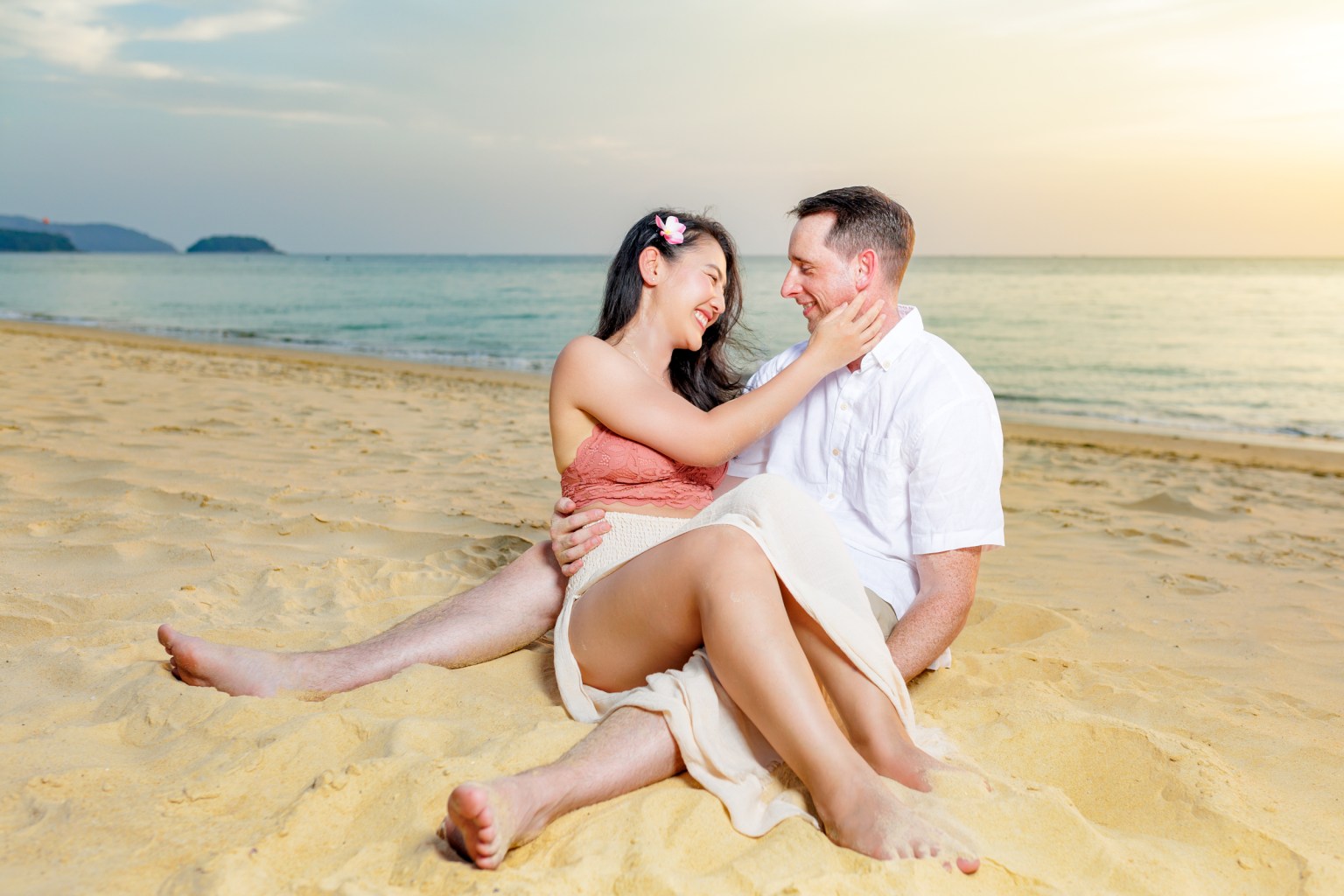 A couple sitting on the beach during sunset, smiling and enjoying a romantic moment together.
