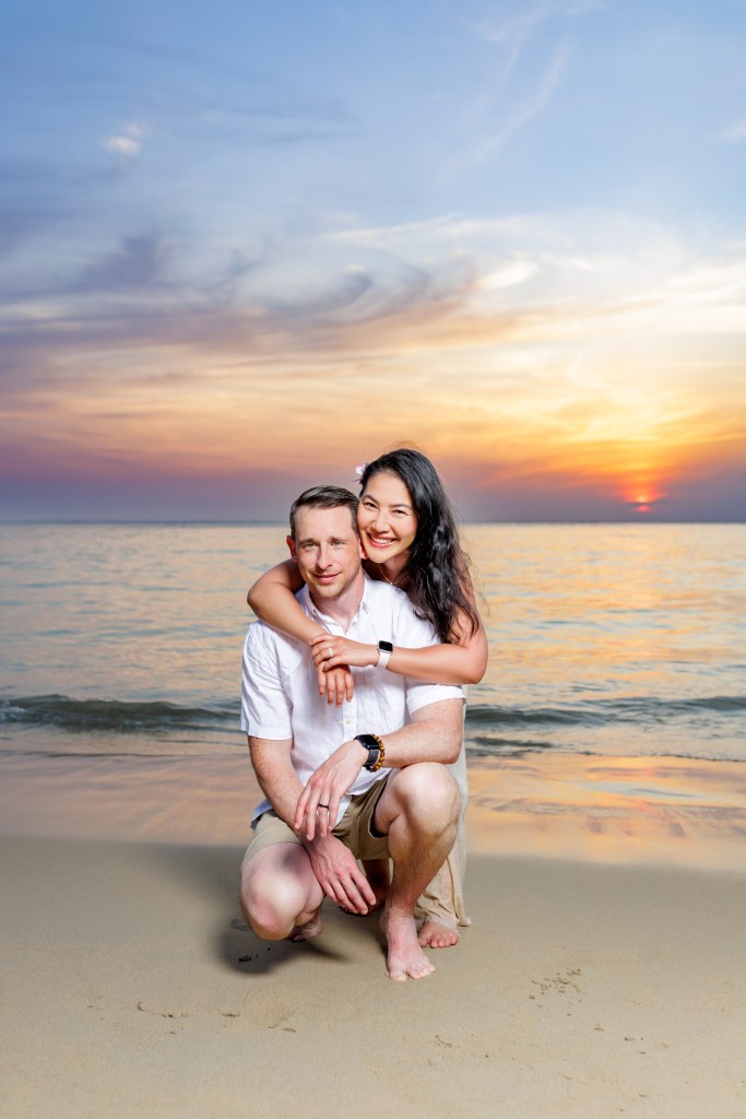 A couple poses joyfully on the beach as sunset at karon beach phuket, with the ocean in the background, capturing a romantic moment during their honeymoon.