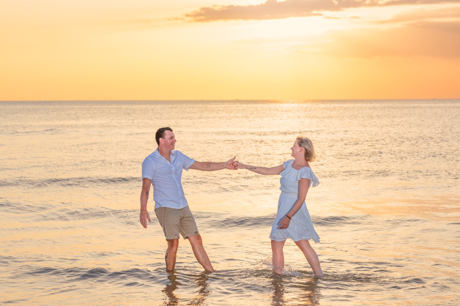 A couple enjoying a romantic moment together in the ocean during sunset, with the water reflecting the golden light at karon beach phuket