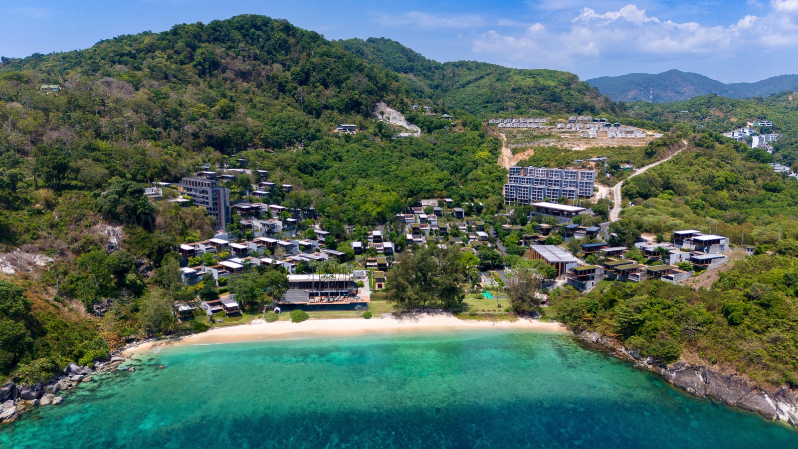 Aerial view of a resort area near kamala beach phuket featuring lush greenery, beach, and modern buildings.