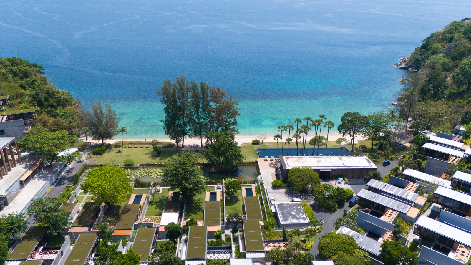 Aerial view of a beach resort in Phuket, showcasing lush greenery, swimming pools, and clear blue waters.
