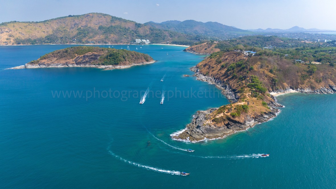 Aerial view of Promthep Cape in Phuket, featuring turquoise waters, hills, and several boats navigating the coastline.
