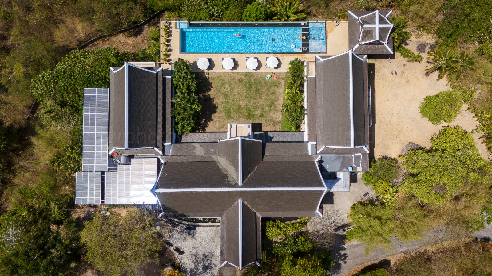 Aerial view of a resort featuring a swimming pool, surrounded by greenery and lounge chairs.