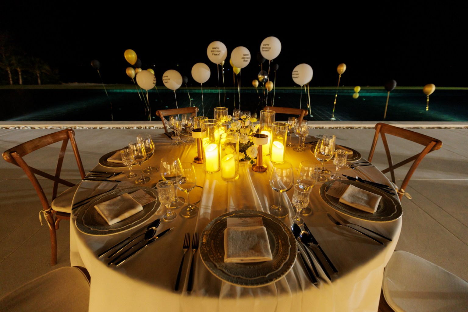 Elegant dinner setup with a beautifully arranged table, glowing candles, and festive balloons at night.