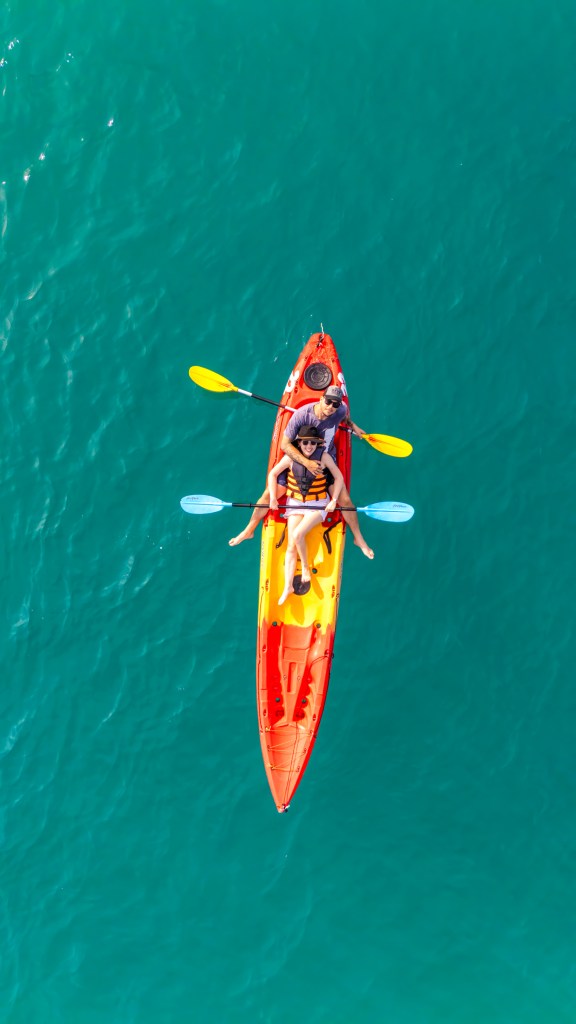 Aerial view of two people kayaking in a colorful kayak on clear turquoise water.