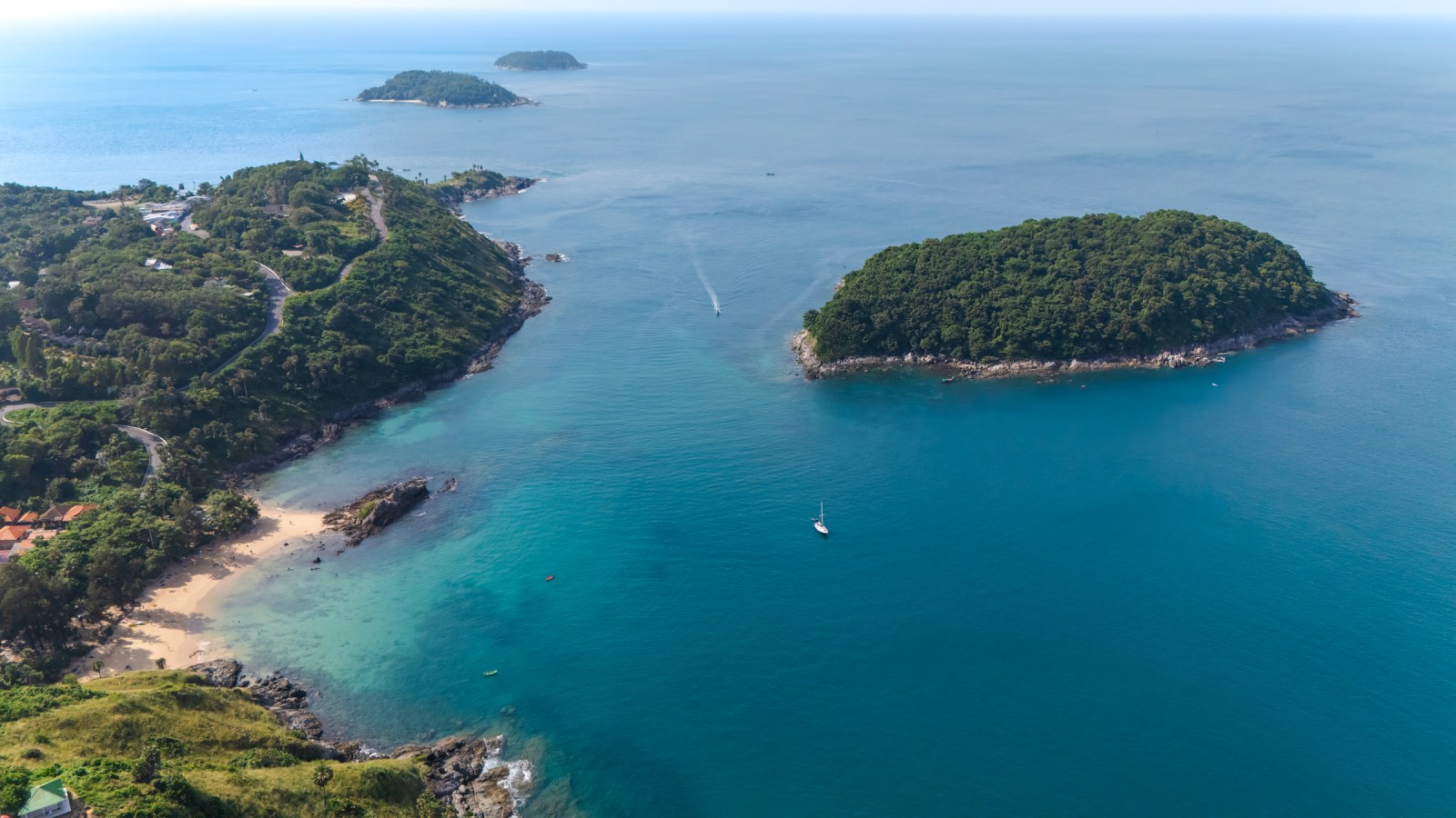 Aerial view of a coastal landscape featuring lush green hills, sandy beaches, and clear turquoise waters, with small boats and islands in the distance.