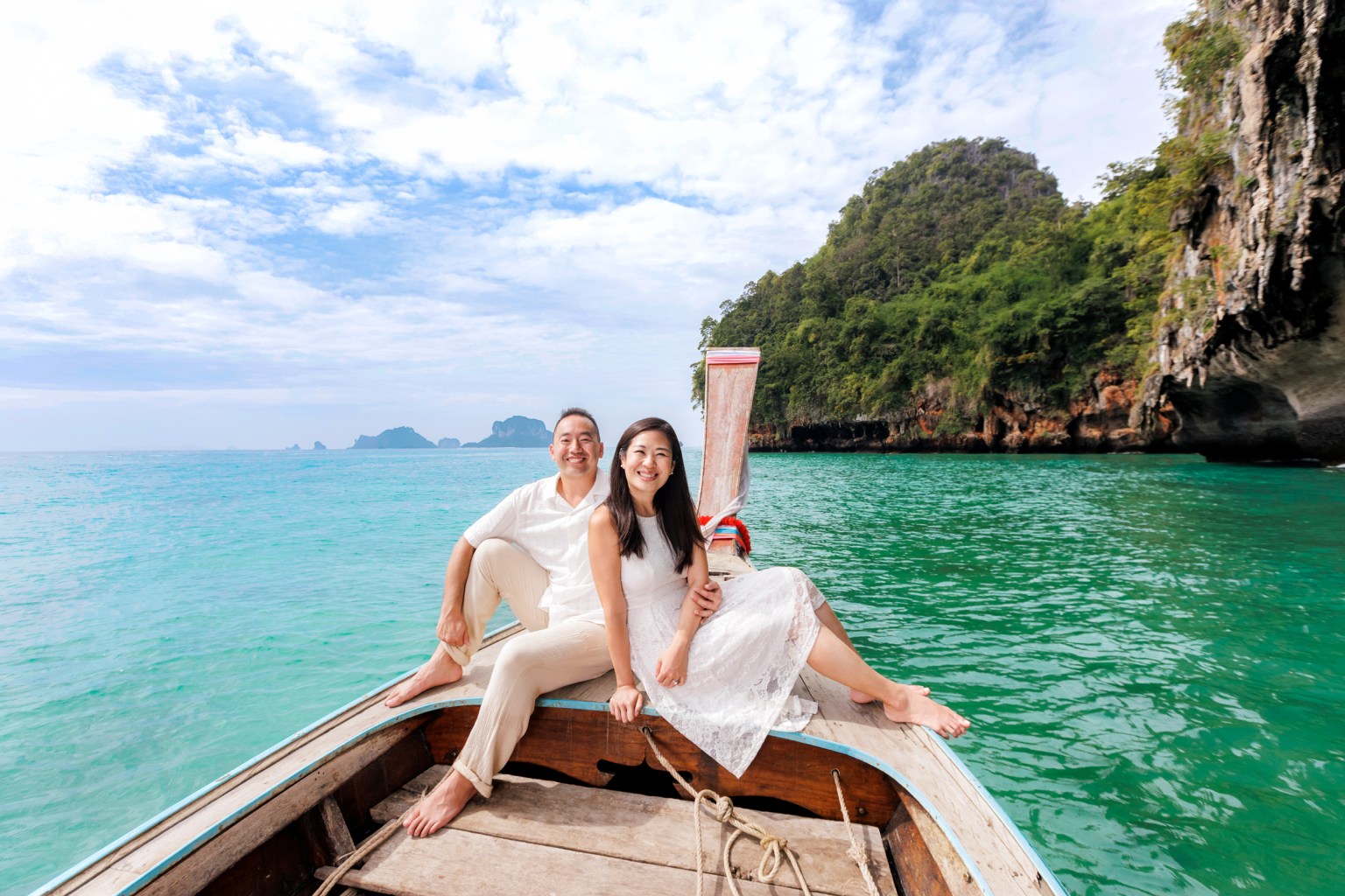 A couple enjoying a romantic moment on a long tail boat, surrounded by turquoise waters and lush green hills in Ao Nang, Krabi.