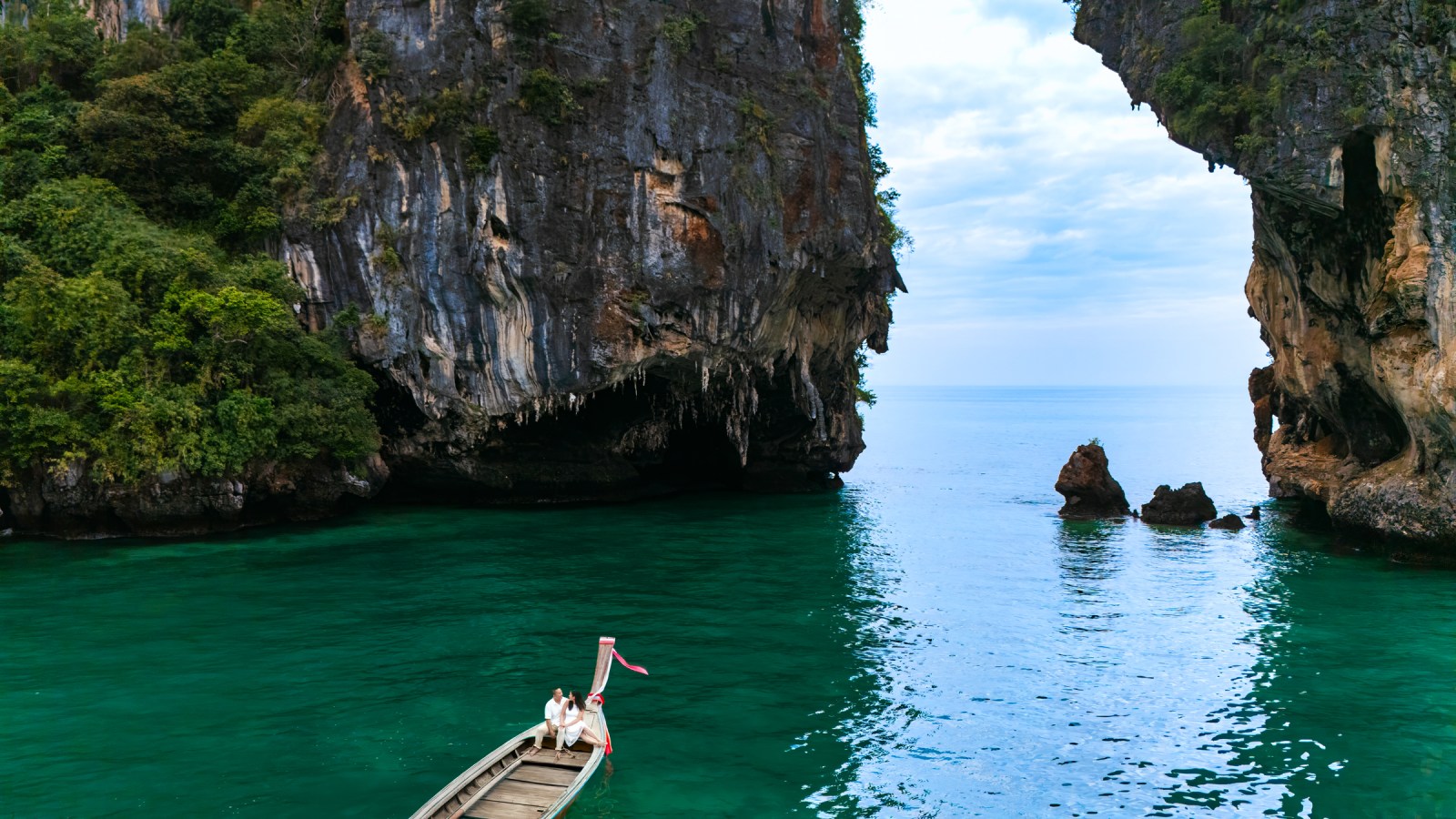 A couple sitting on a boat in turquoise waters, surrounded by towering cliffs and rock formations in a scenic bay.
