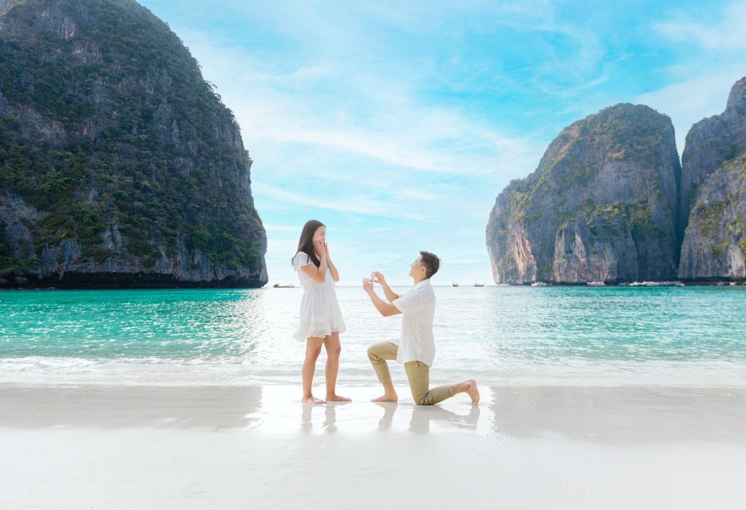 A man proposing to a woman on a beach, surrounded by stunning cliffs and clear water at maya bay phi phi island krabi thailand.