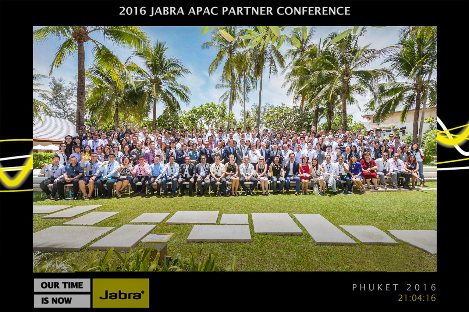 event photography Group photo of attendees at the 2016 Jabra APAC Partner Conference held in Phuket, featuring a large gathering of people seated on a lawn surrounded by palm trees.