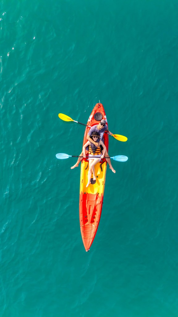Two people kayaking on a bright orange and yellow kayak in clear, turquoise water.