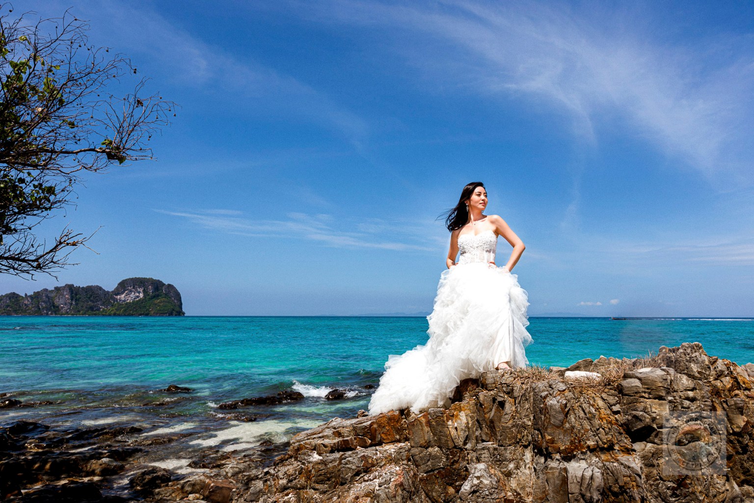 Bride in a white wedding dress standing on a rock with a scenic ocean background at Bamboo Island, Krabi.