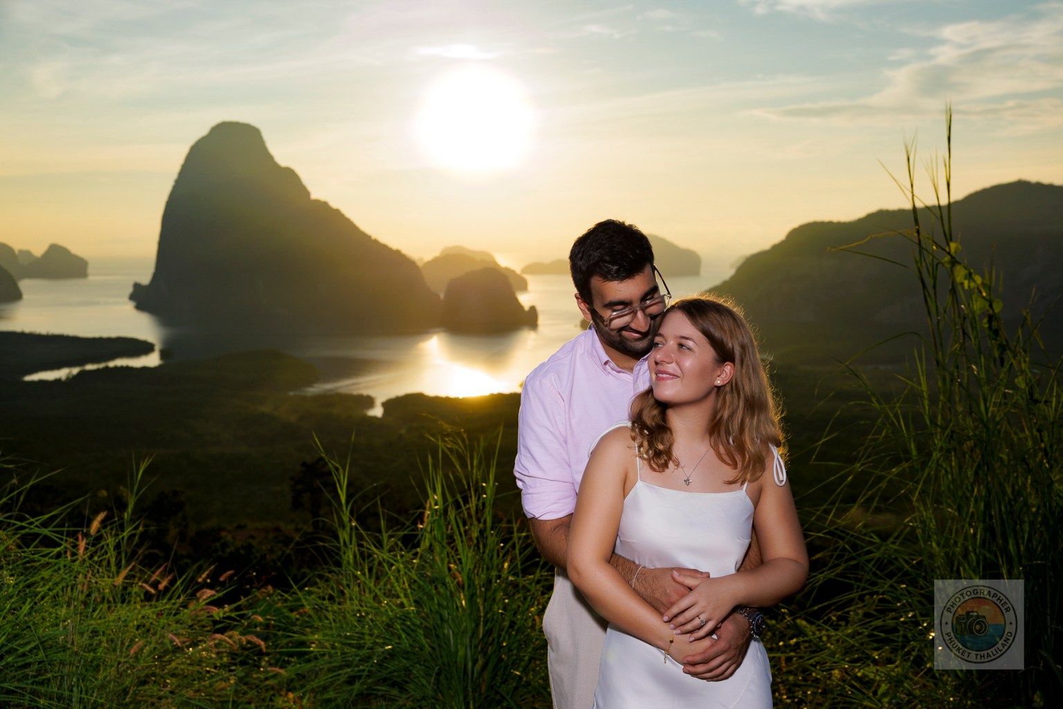 A couple embraces with a scenic mountain and sunset background, capturing a romantic moment in nature.