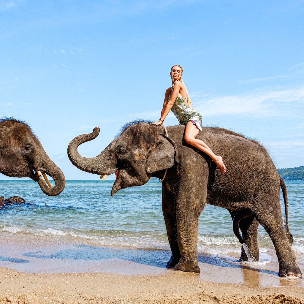 A woman riding an elephant on a beach, with another elephant nearby for photo shooting in phuket , under a clear blue sky 